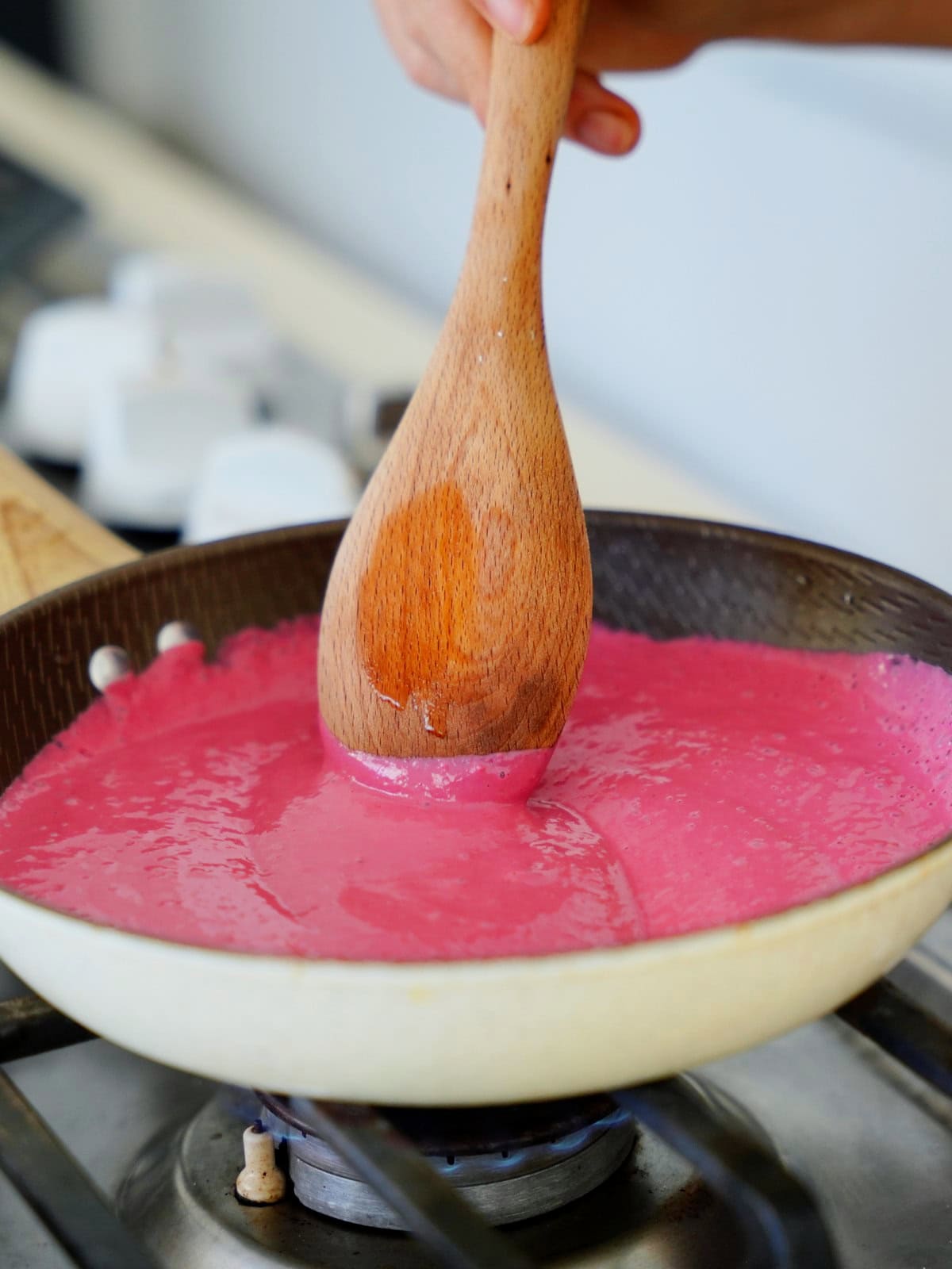 Wooden spoon stirring beetroot sauce in saucepan