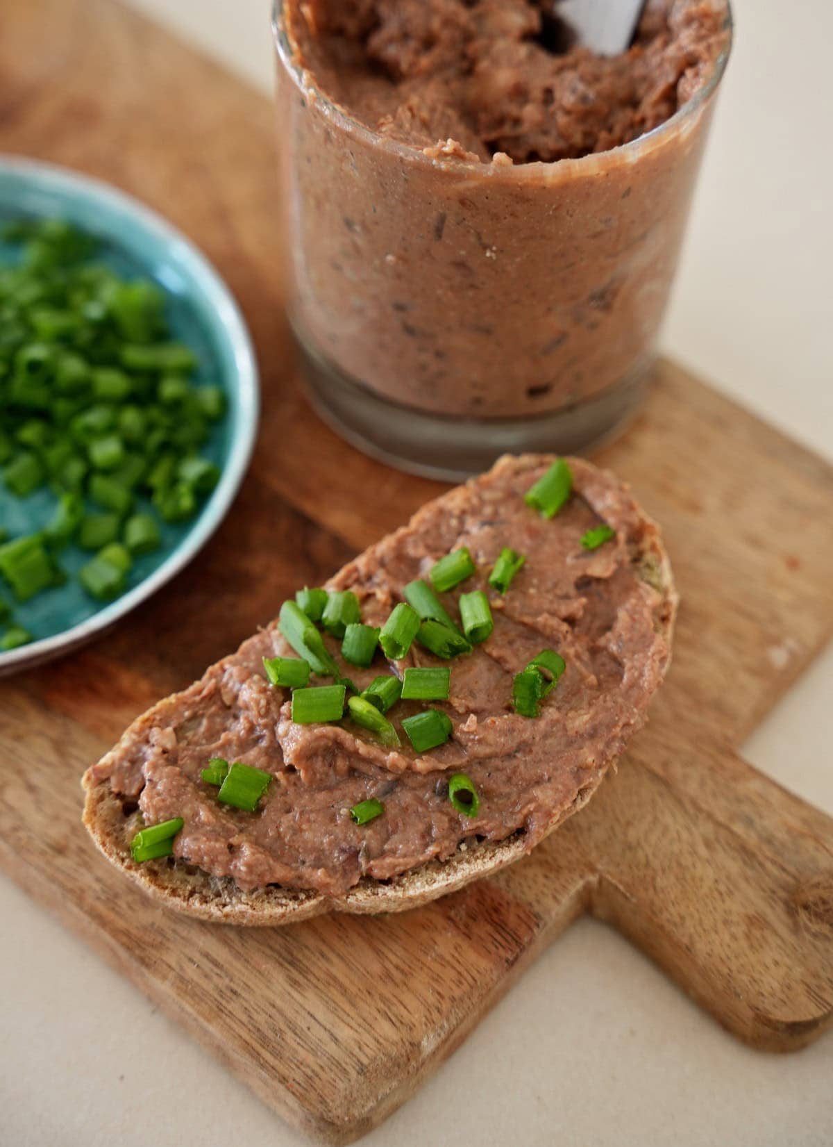 vegan liverwurst on a slice of bread with chives and a jar behind it