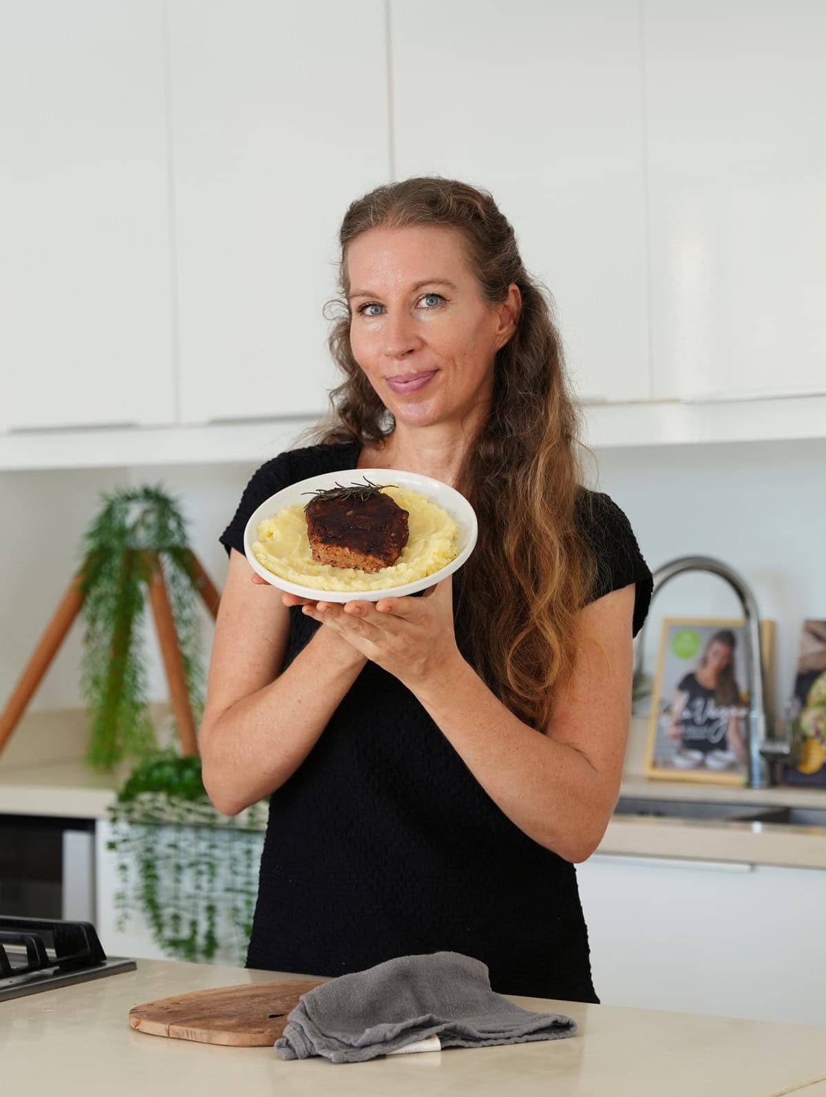 Michaela Vais in a bright kitchen holding a plate with vegan steak and mashed potatoes