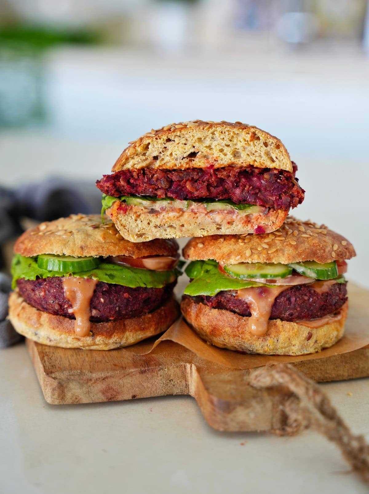 Three beet burgers on a wooden board the one on top showing the inside of the patty