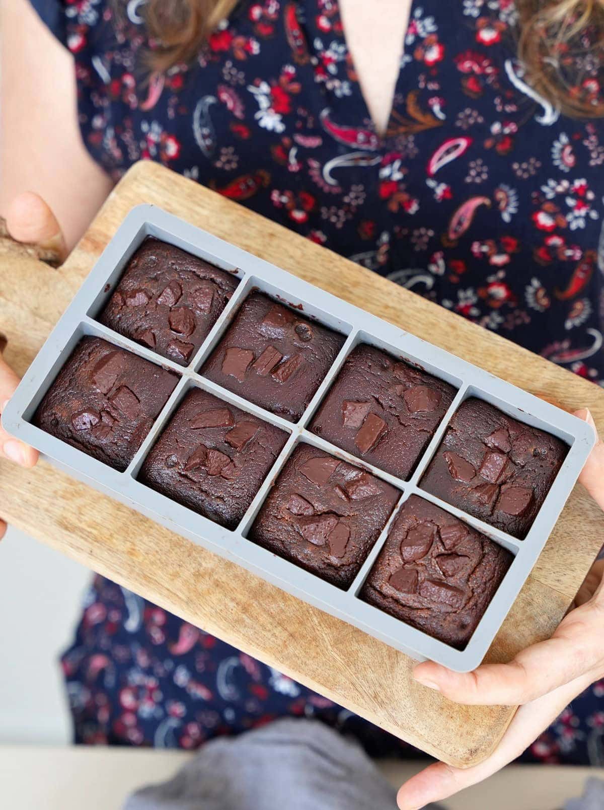 Woman holding 6 red lentil brownies in silicone mold on a wooden board