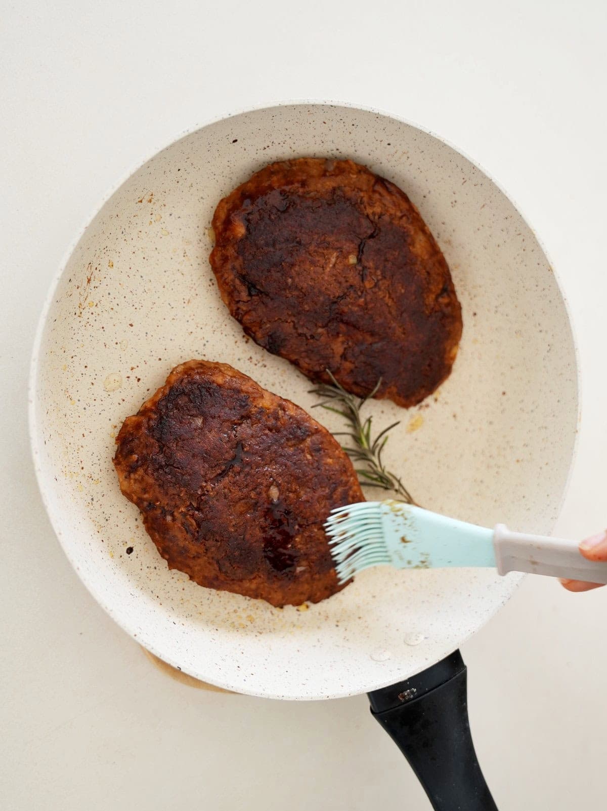 brushing two white bean steaks with vegan marinade in white skillet