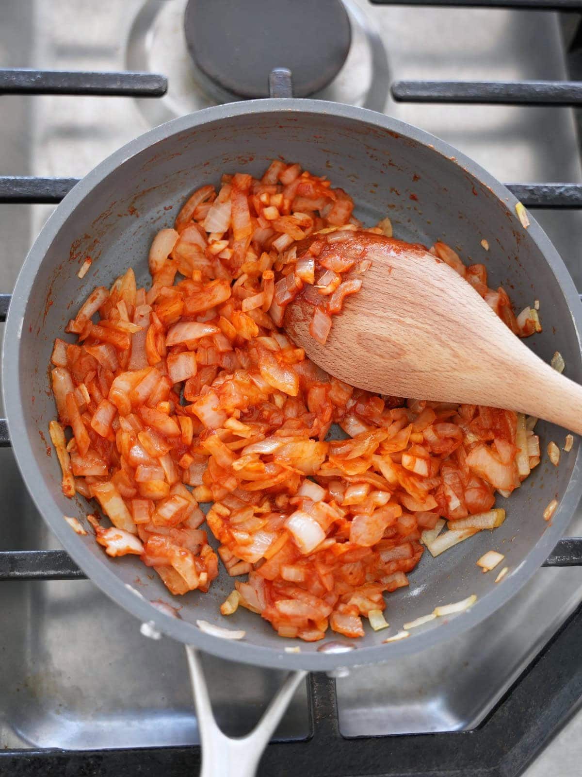 diced onions with tomato paste in skillet with wooden spoon