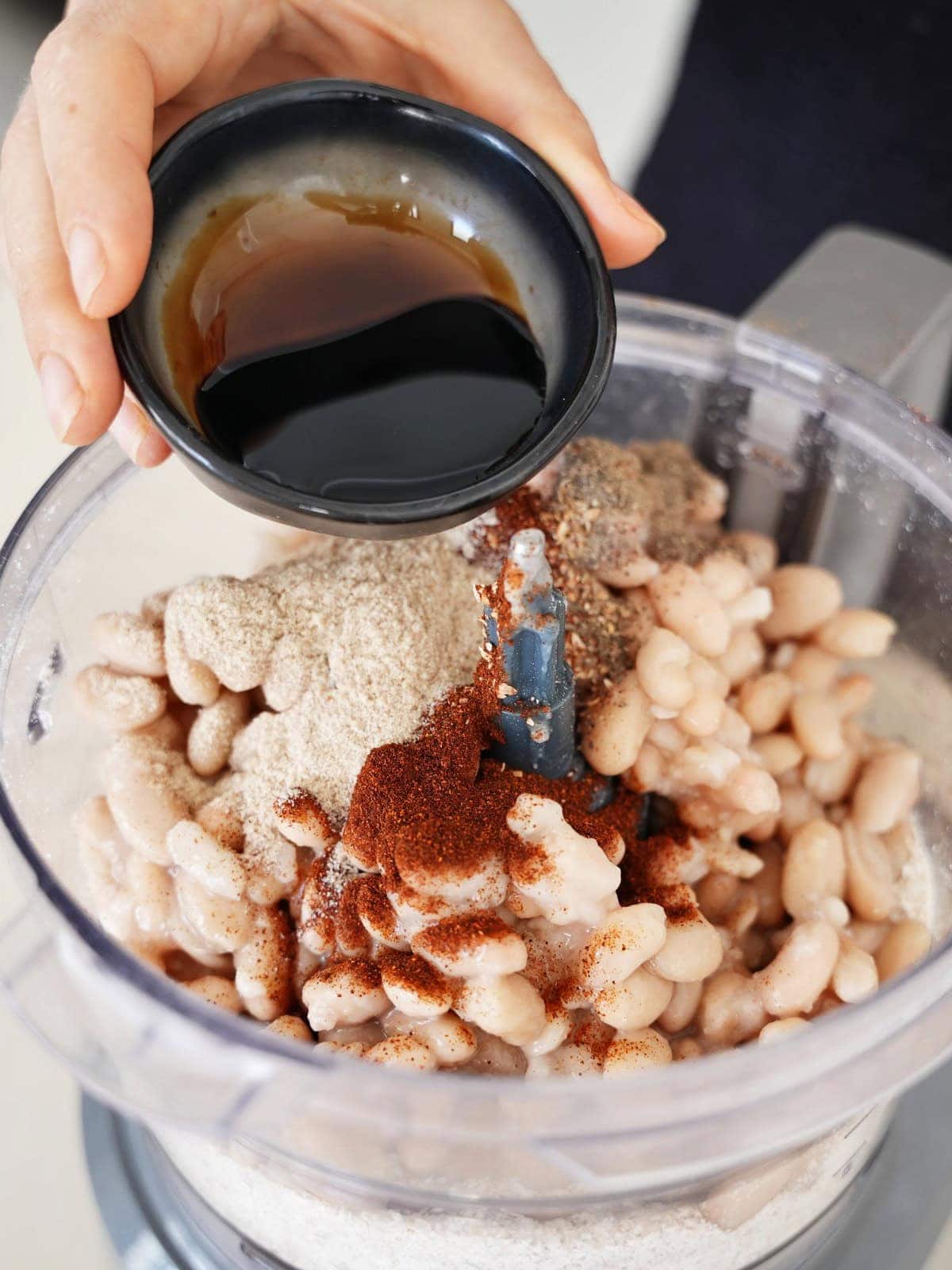 pouring soy sauce into food processor with beans and spices