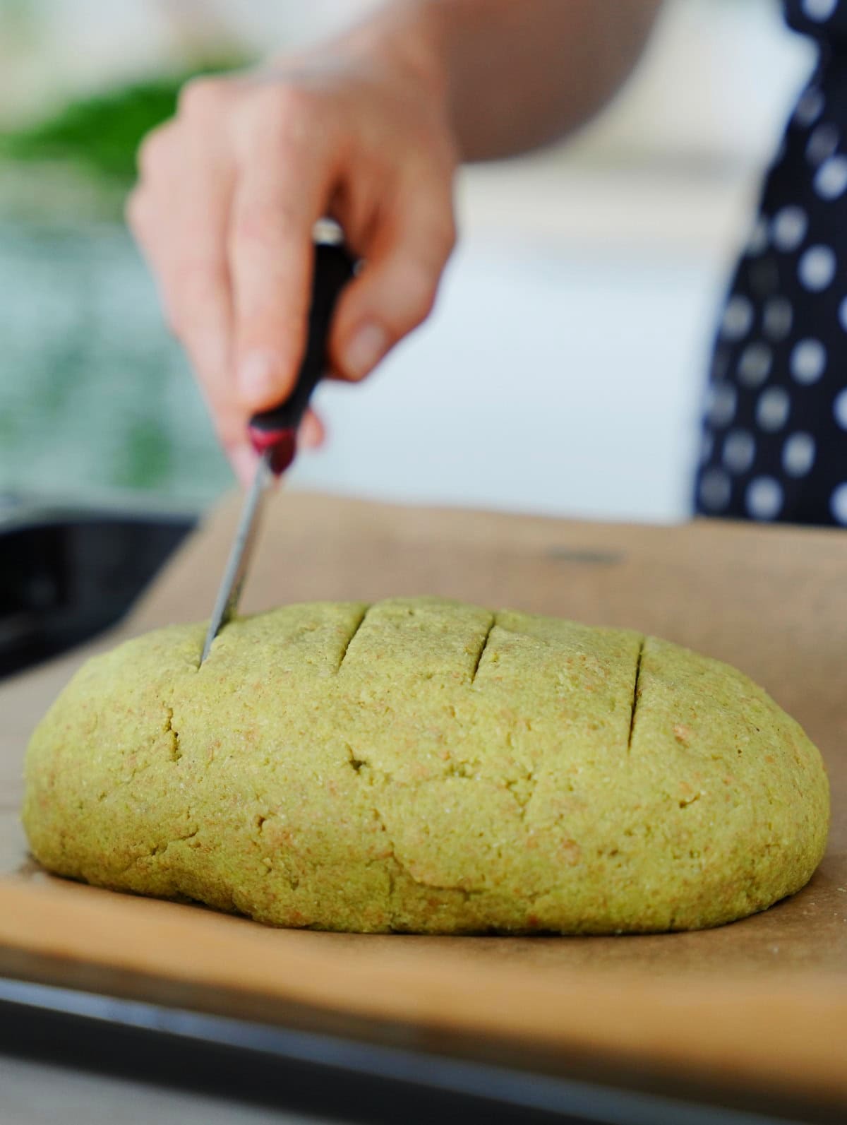 scoring green loaf on lined baking sheet